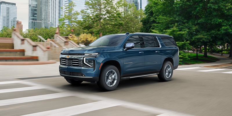 Blue Chevrolet Suburban driving through a city intersection.